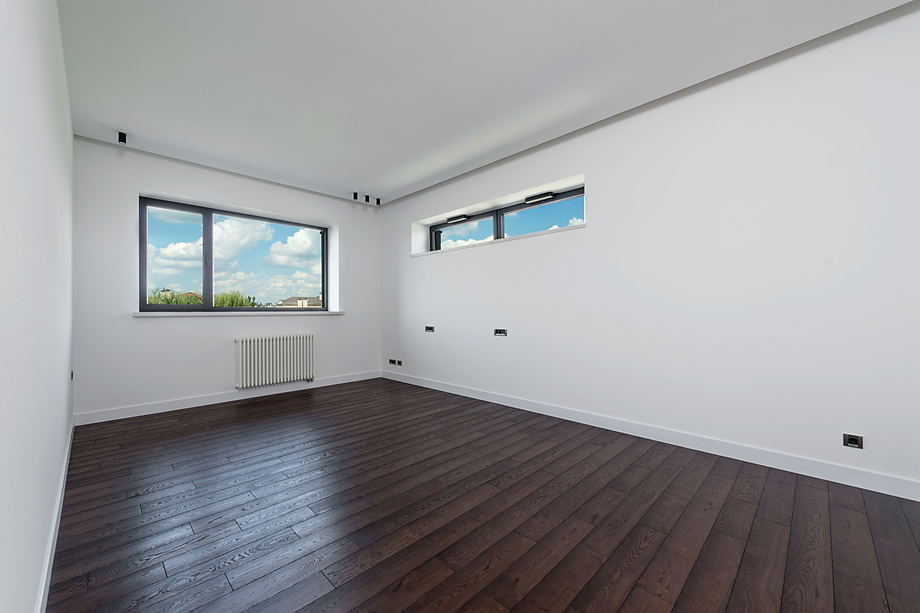 Lege woonkamer met een pas gelegde donkere houten vloer en daglicht uit een raamstrook